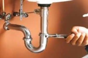 A plumber loosens a pipe under a sink with a pair of channel lock pliers