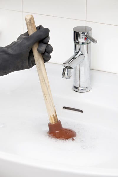A homeowner tries to unclog a sink with a plunger
