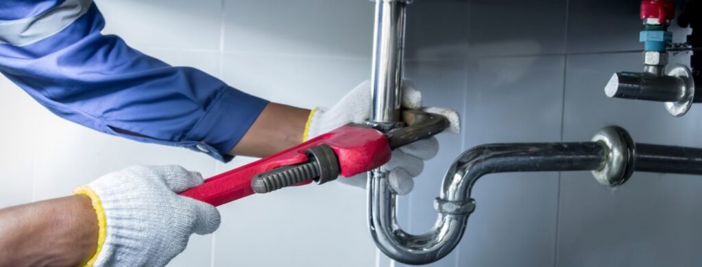 A plumber is working on fixing a pipe under a sink.